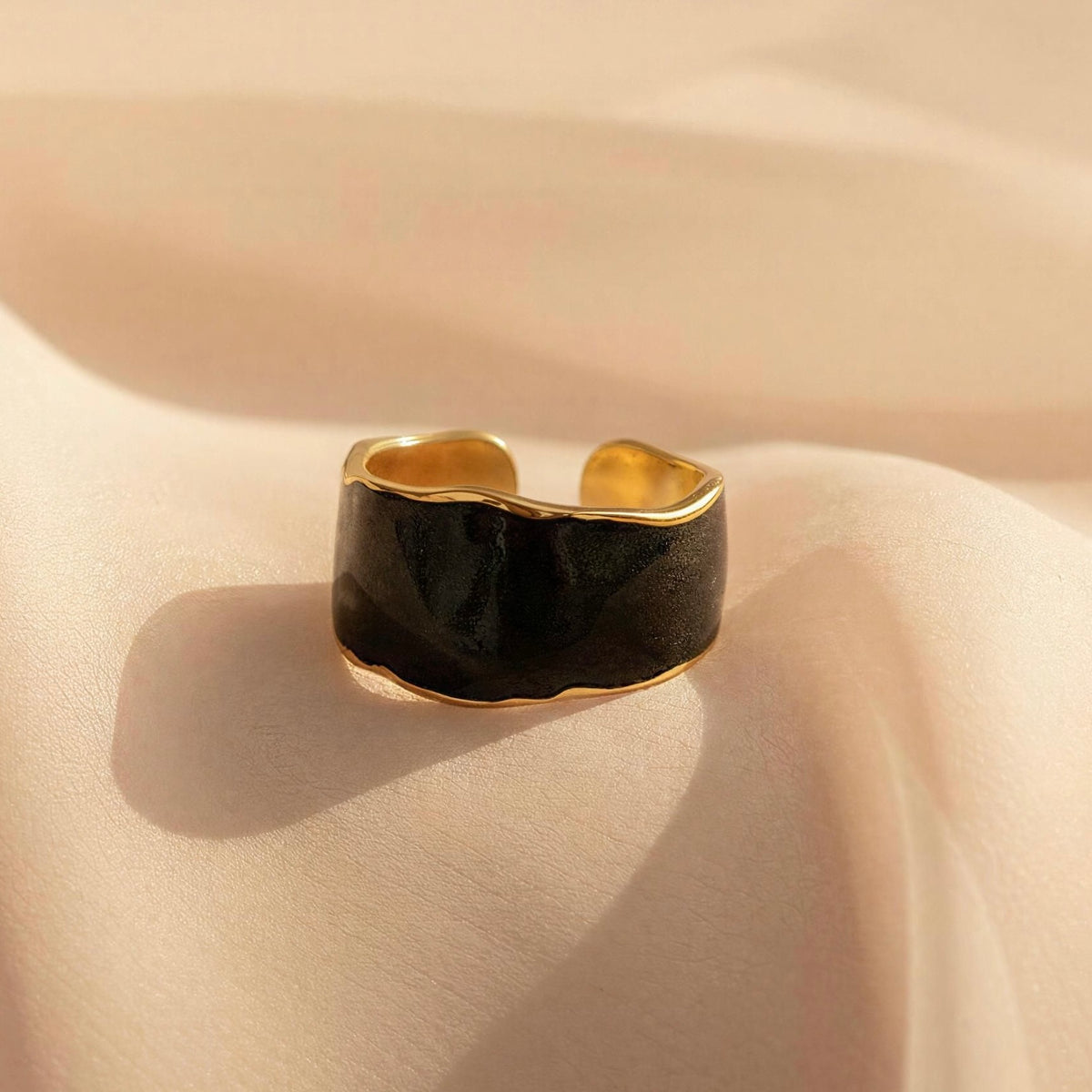 The Duna Ring – Ónice from Chica Chica Jewelry.  A wide, chunky ring with a glossy black center and polished gold-toned edges, resting on draped beige fabric.