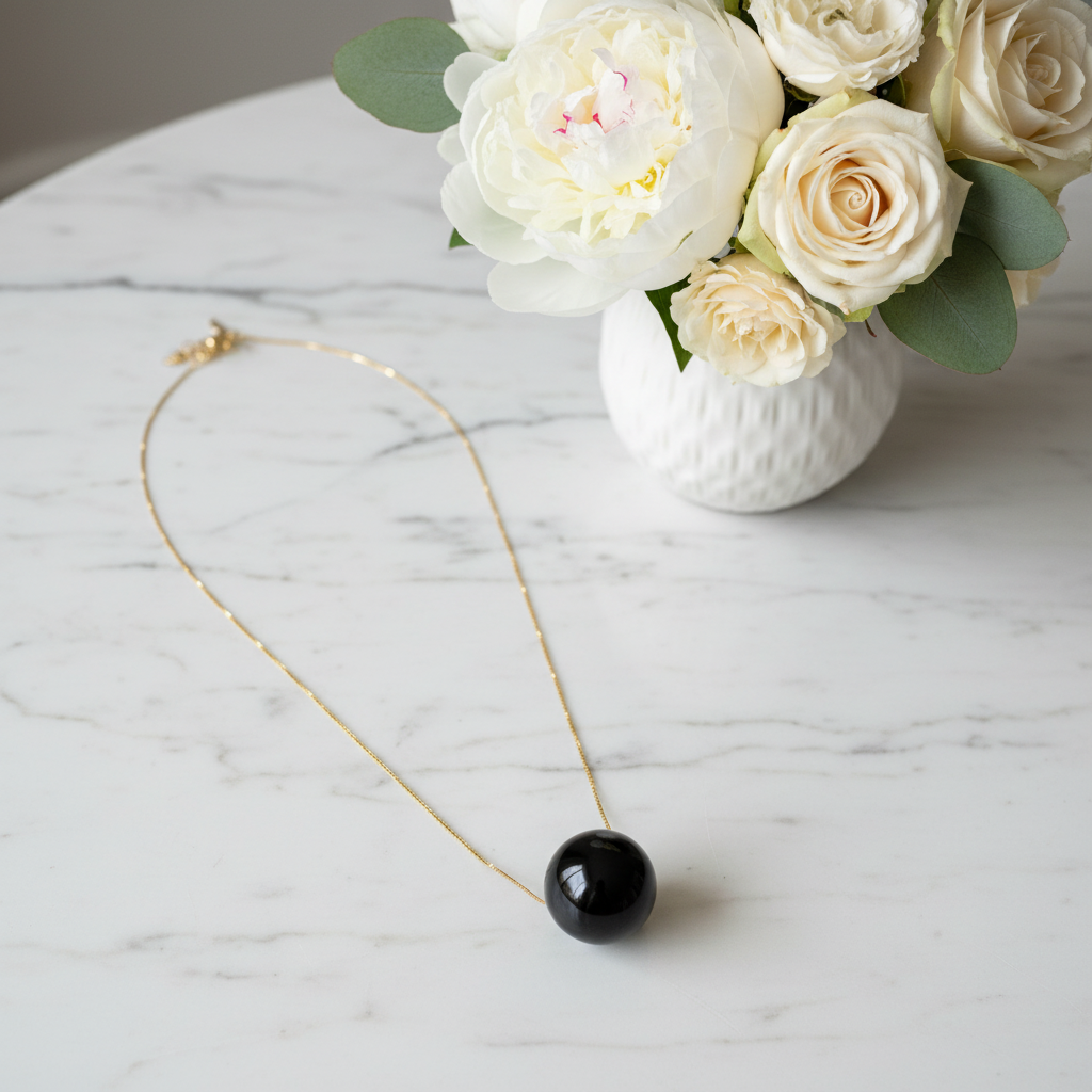 The Ebony Bead Necklace on a marble surface next to a vase of white roses.