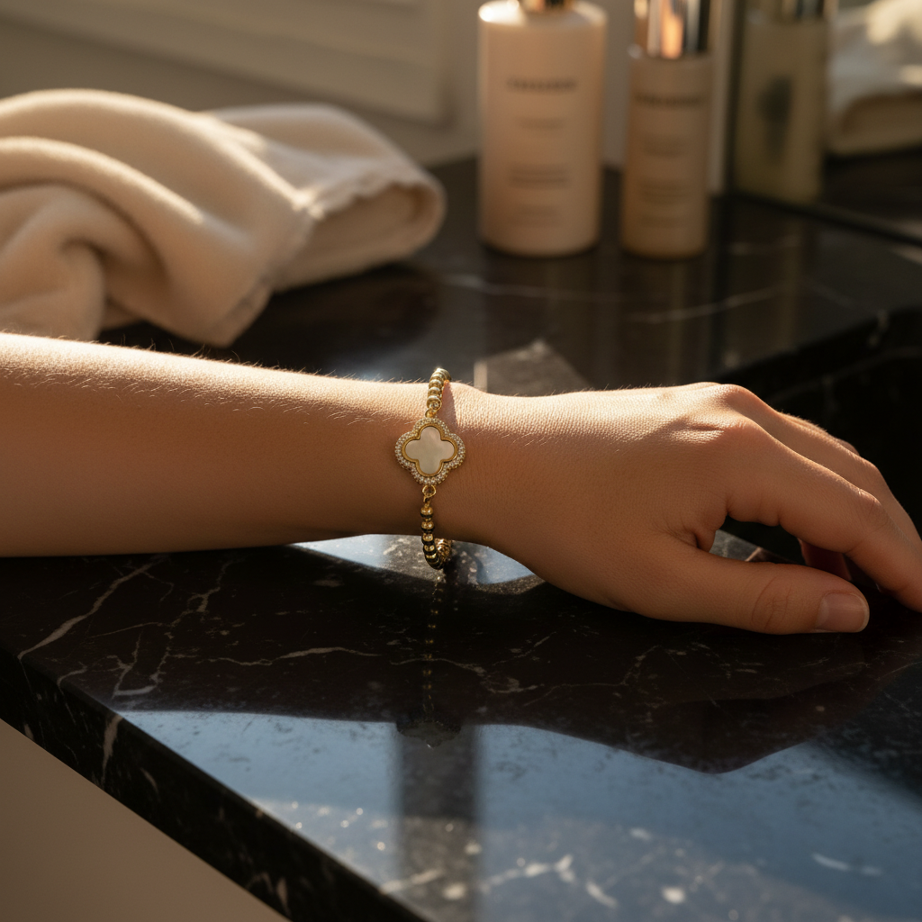 Hand wearing a gold bracelet on a dark marble surface with skincare products in the background
