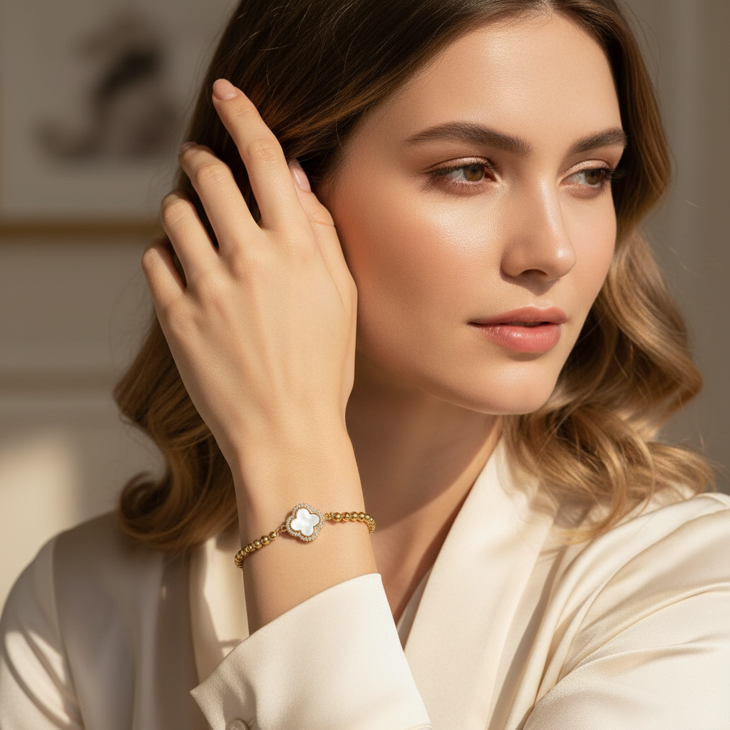 Woman wearing a gold bracelet with a white flower design, posing with one hand by her face.