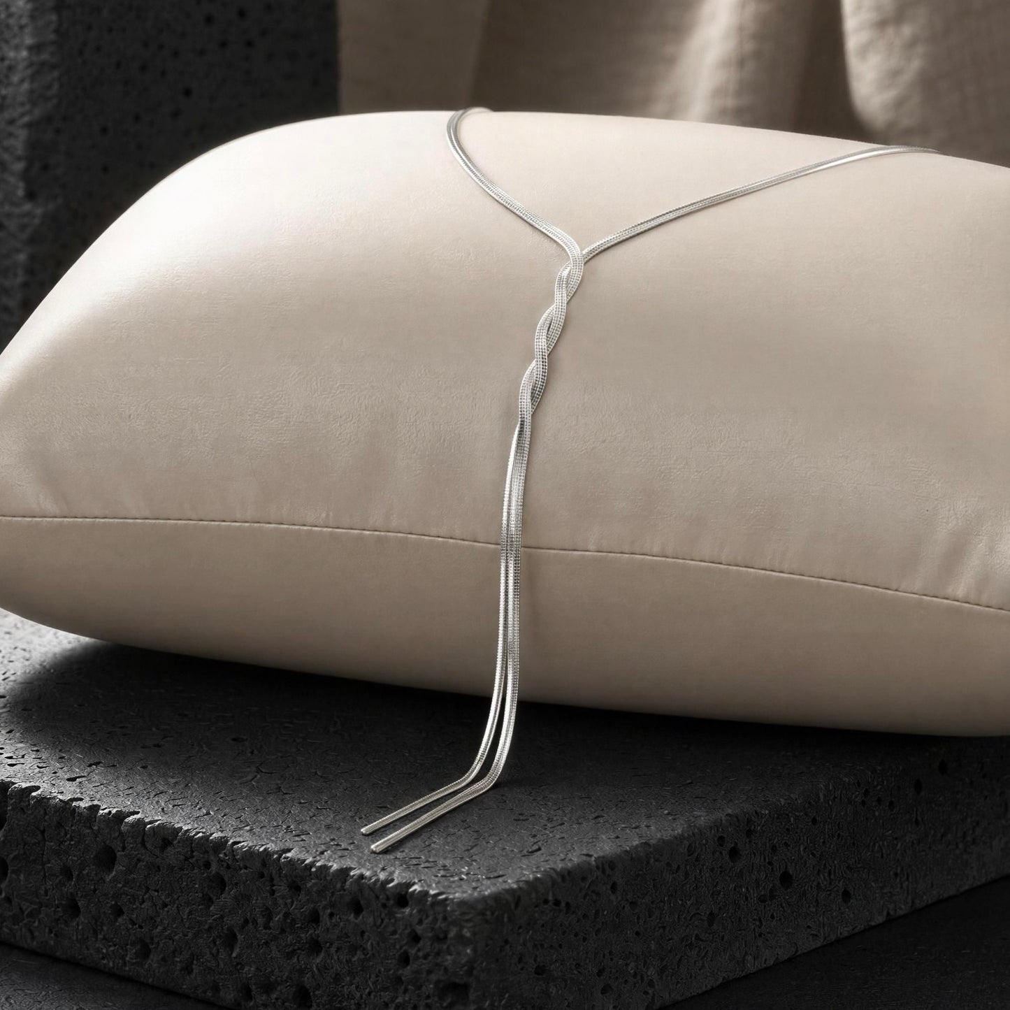 Silver necklace draped over a beige pillow on a dark surface