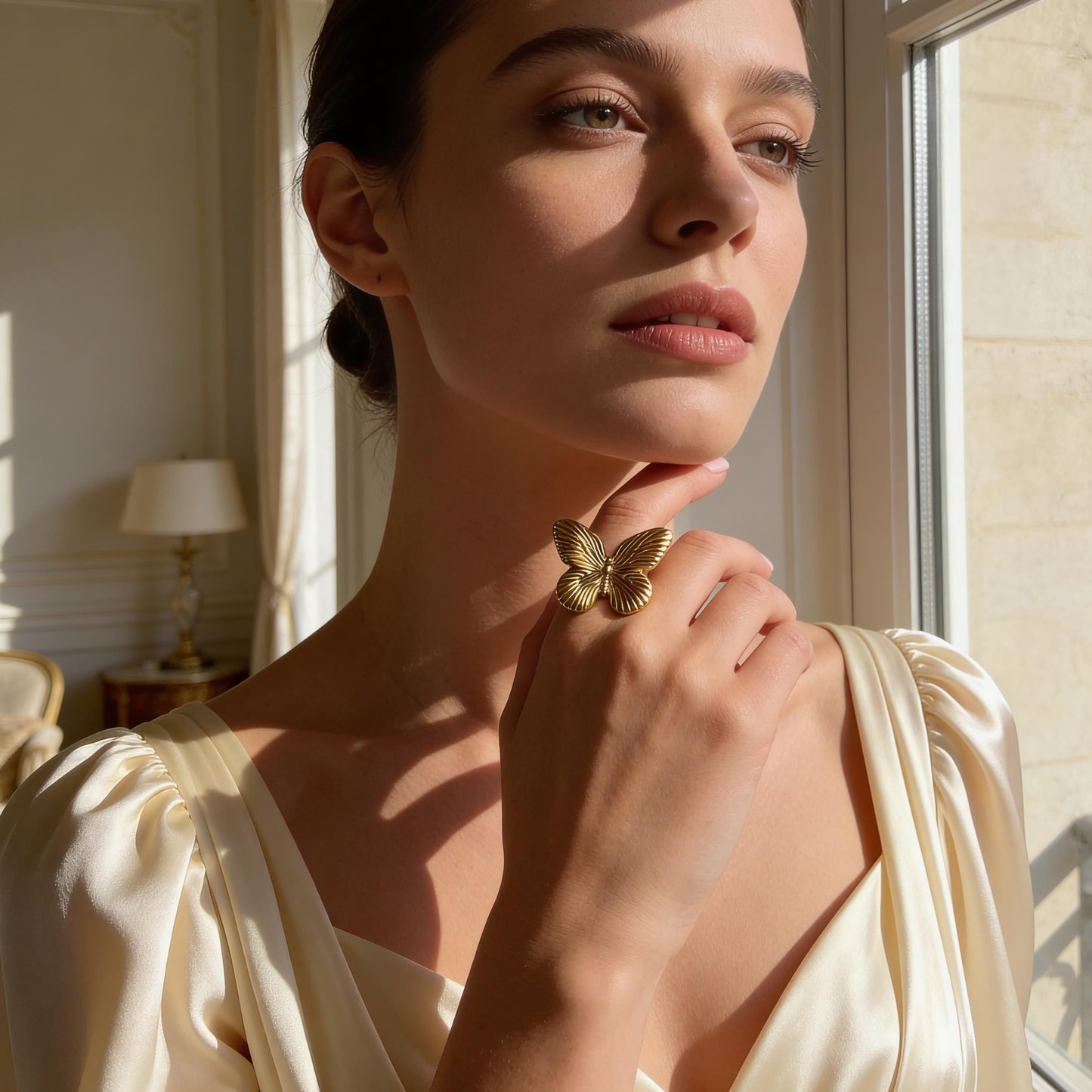 Woman in a cream-colored dress with a the Forever Flutter Ring - Gold  in a sunlit room.