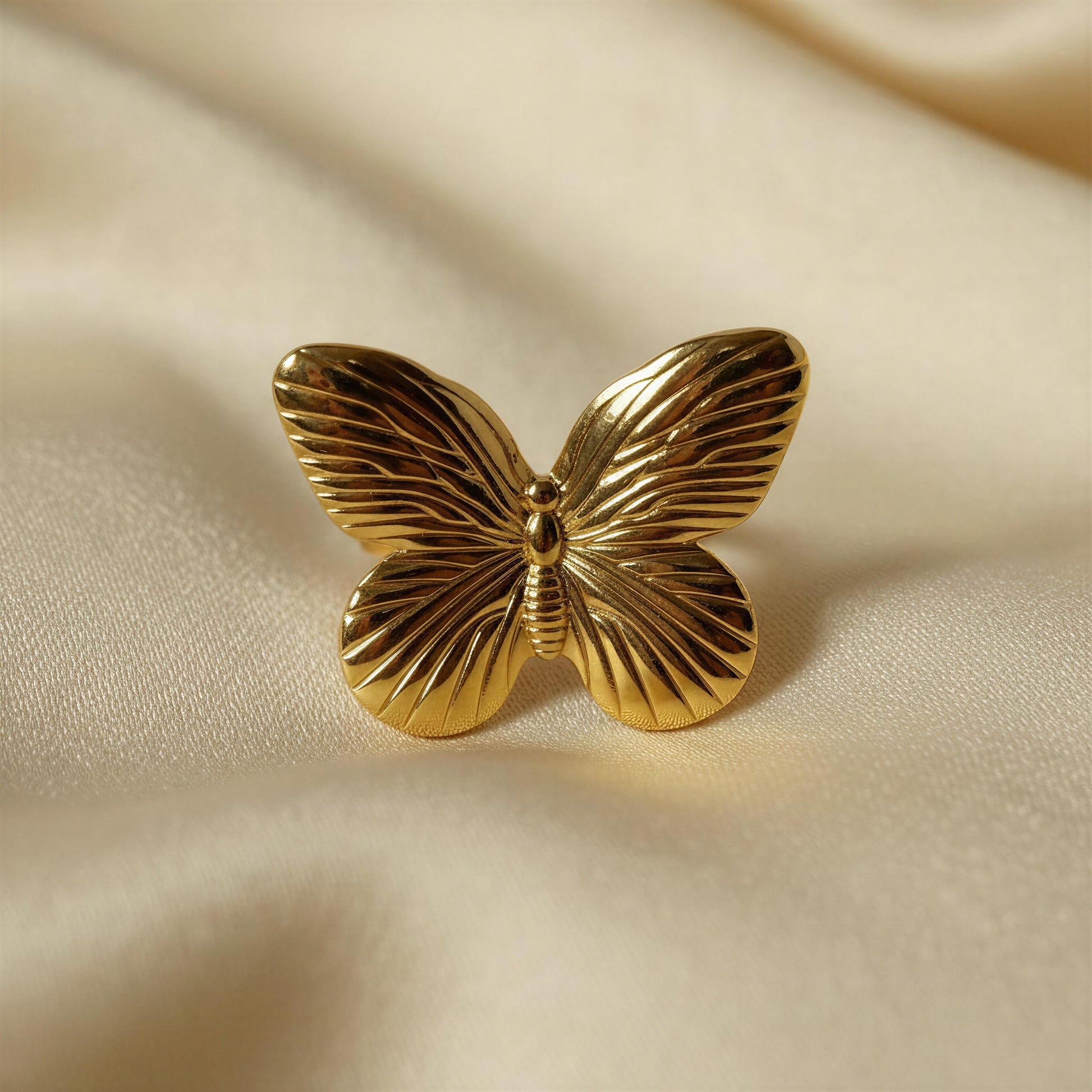 the Forever Flutter Ring - Gold  in a beige fabric background