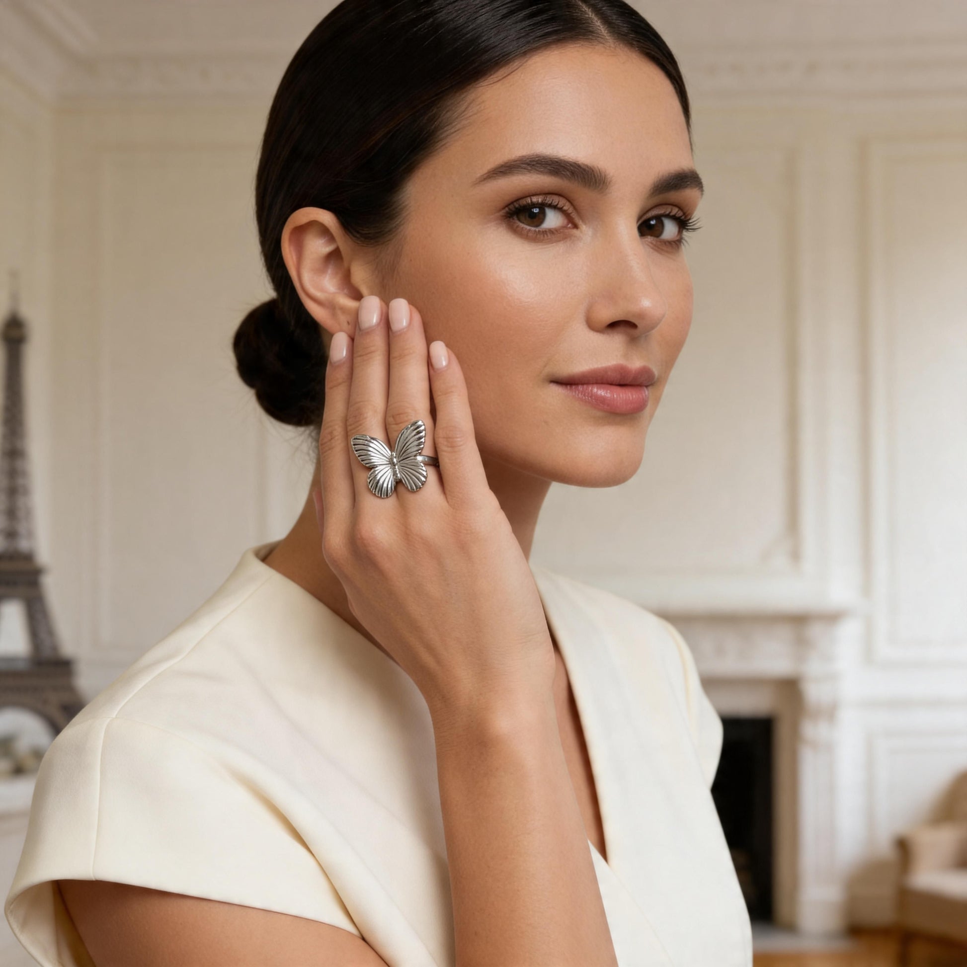 Woman wearing a butterfly-shaped ring in an elegant indoor setting with the Eiffel Tower wall paper  in the background.