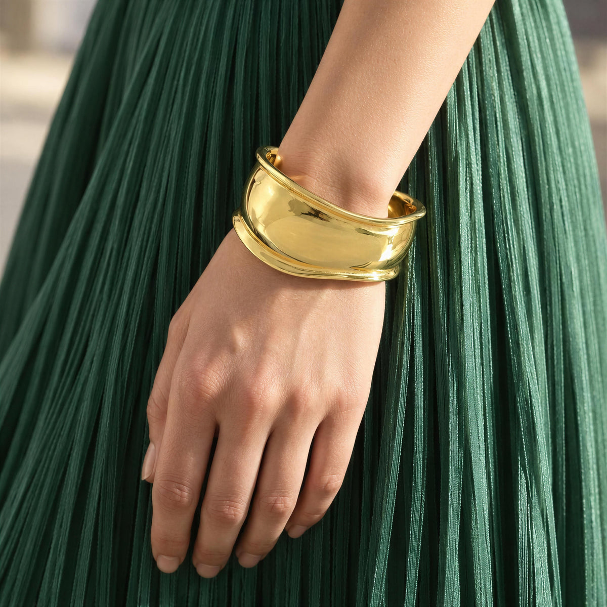 Close-up of Forma Gold cuff bracelet worn with emerald green pleated dress