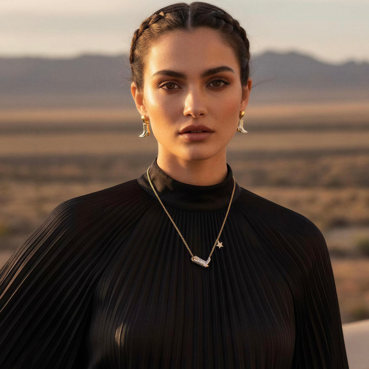 Model wearing the Frontier Boot Jewelry Set from Chica Chica Jewelry and a black luxurious silk pleated dress by a hotel promenade in desert.