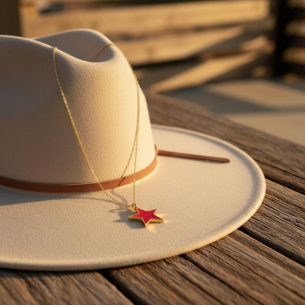 Fuchsia Star Necklace from Chica Chica Jewelry, a 18K gold-plated fuchsia  star necklace draped over a cream-colored cowboy hat on a wooden table.