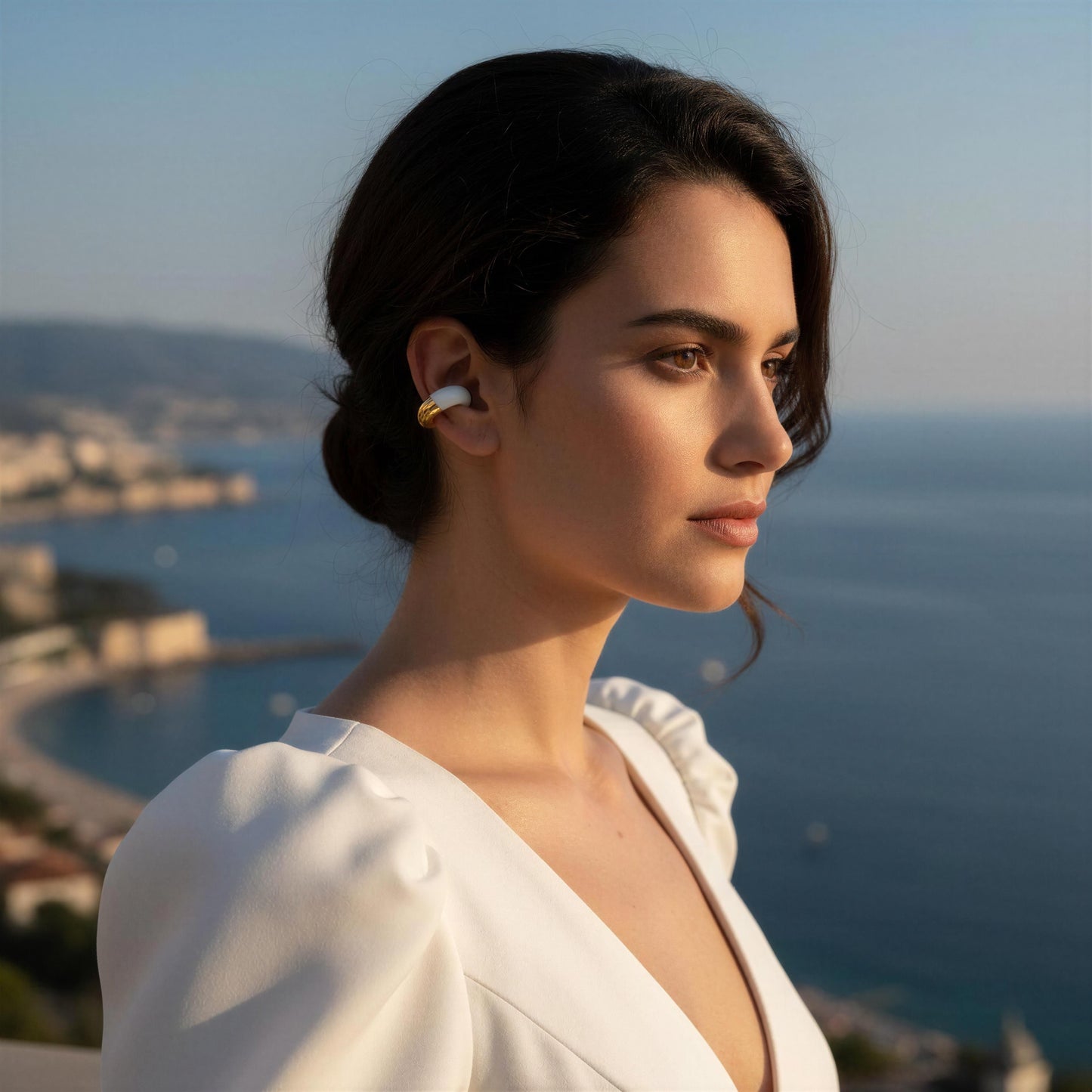 Woman wearing the Gatsby Arc Ear Cuff in Milky White  with a scenic background of water and buildings.