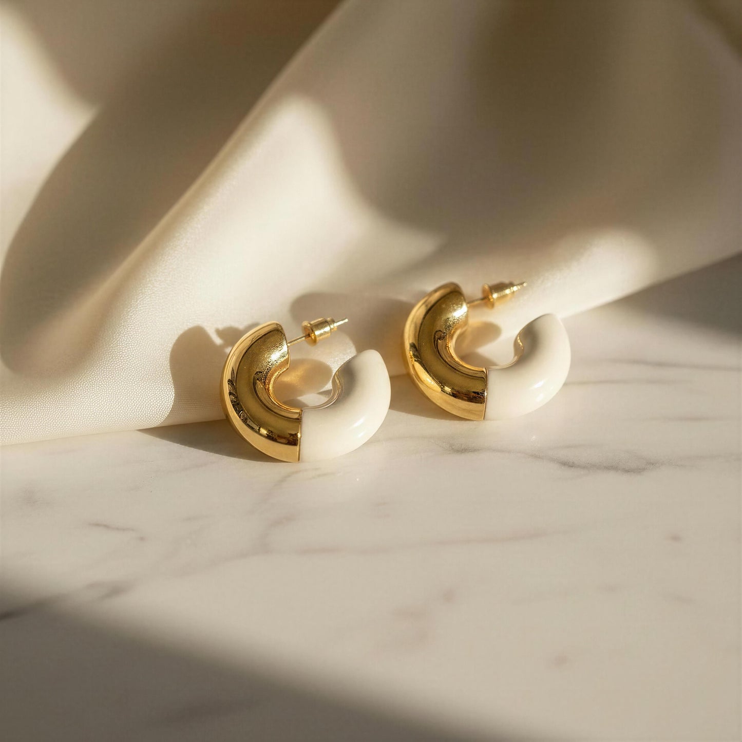 Gold hoop earrings on a marble surface with soft shadows