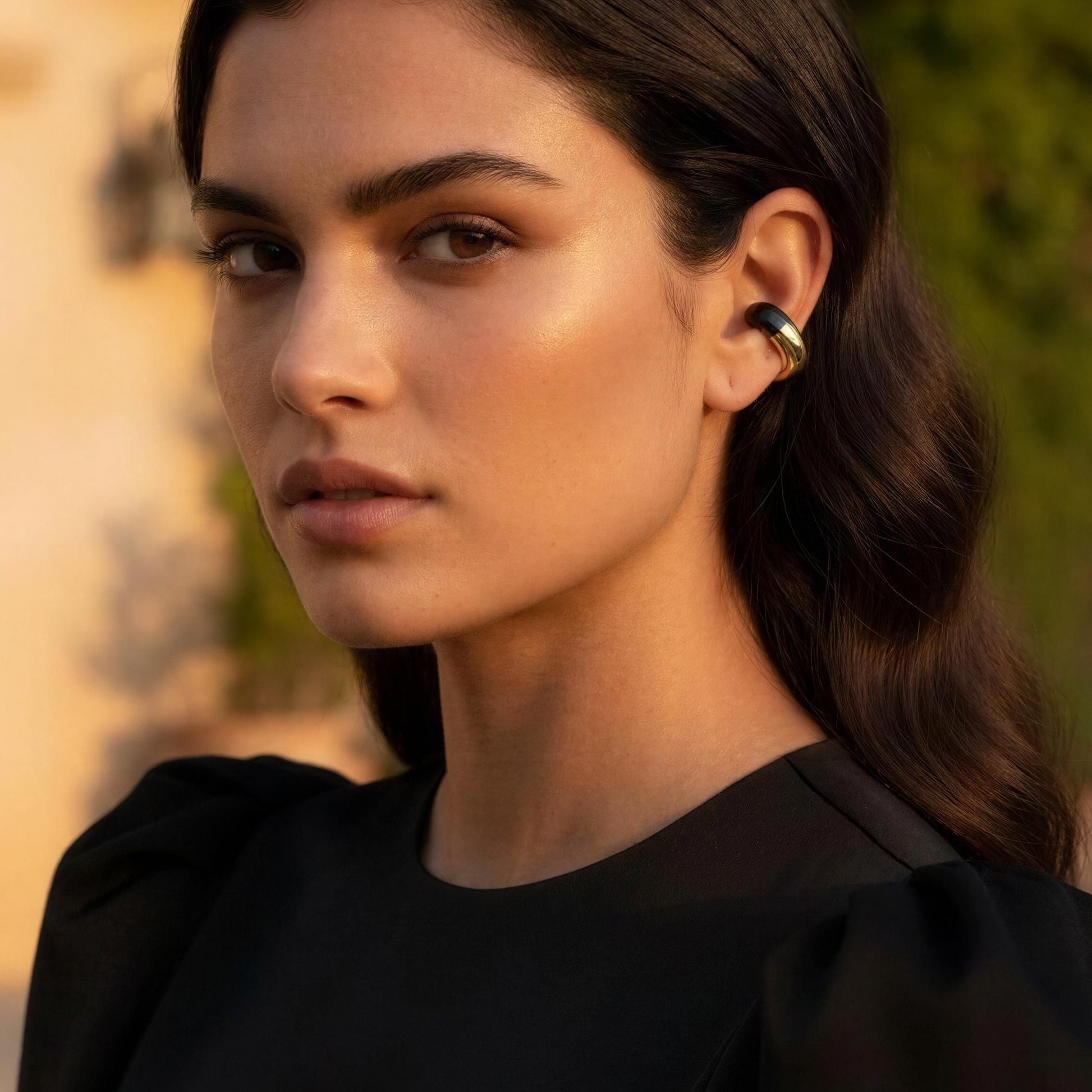 Woman in a black top standing outdoors with a blurred background wearing the Gatsby Ear Cuff in Onyx.