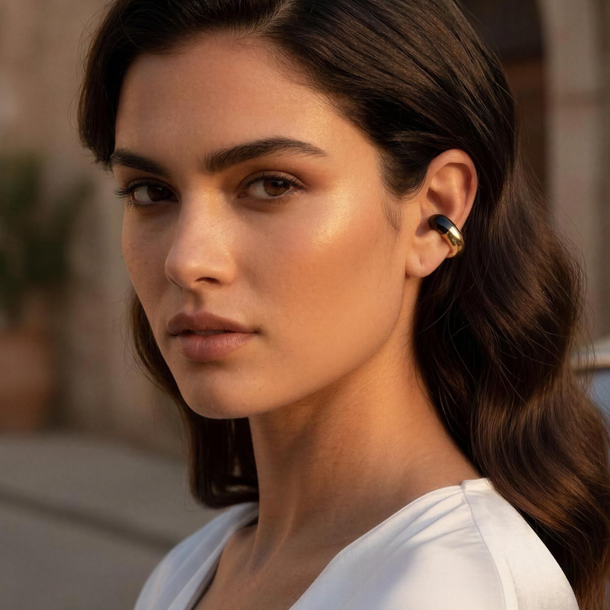 Woman in a white top standing outdoors with a blurred background and the Gatsby Ear Cuff in Onyx
