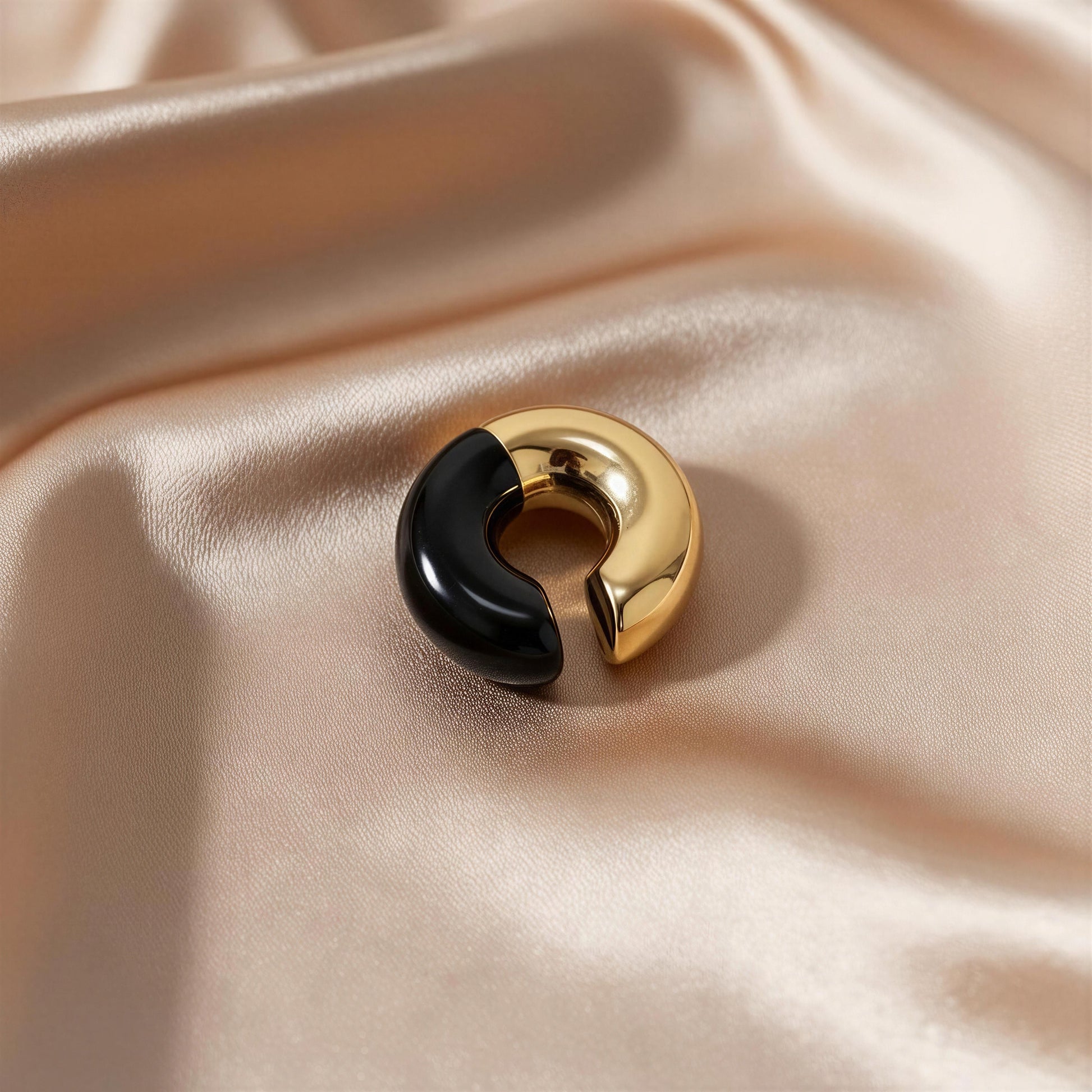 Gold and black ear cuff on a beige satin background