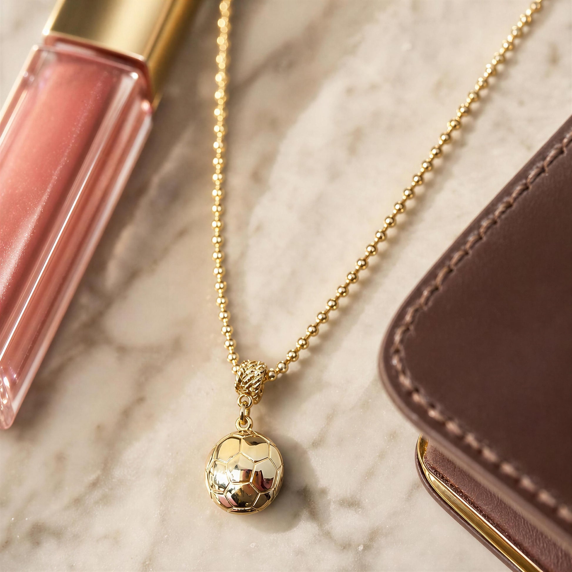 The Gol Dorado Necklace on a marble surface next to pink lip gloss and a brown leather case.