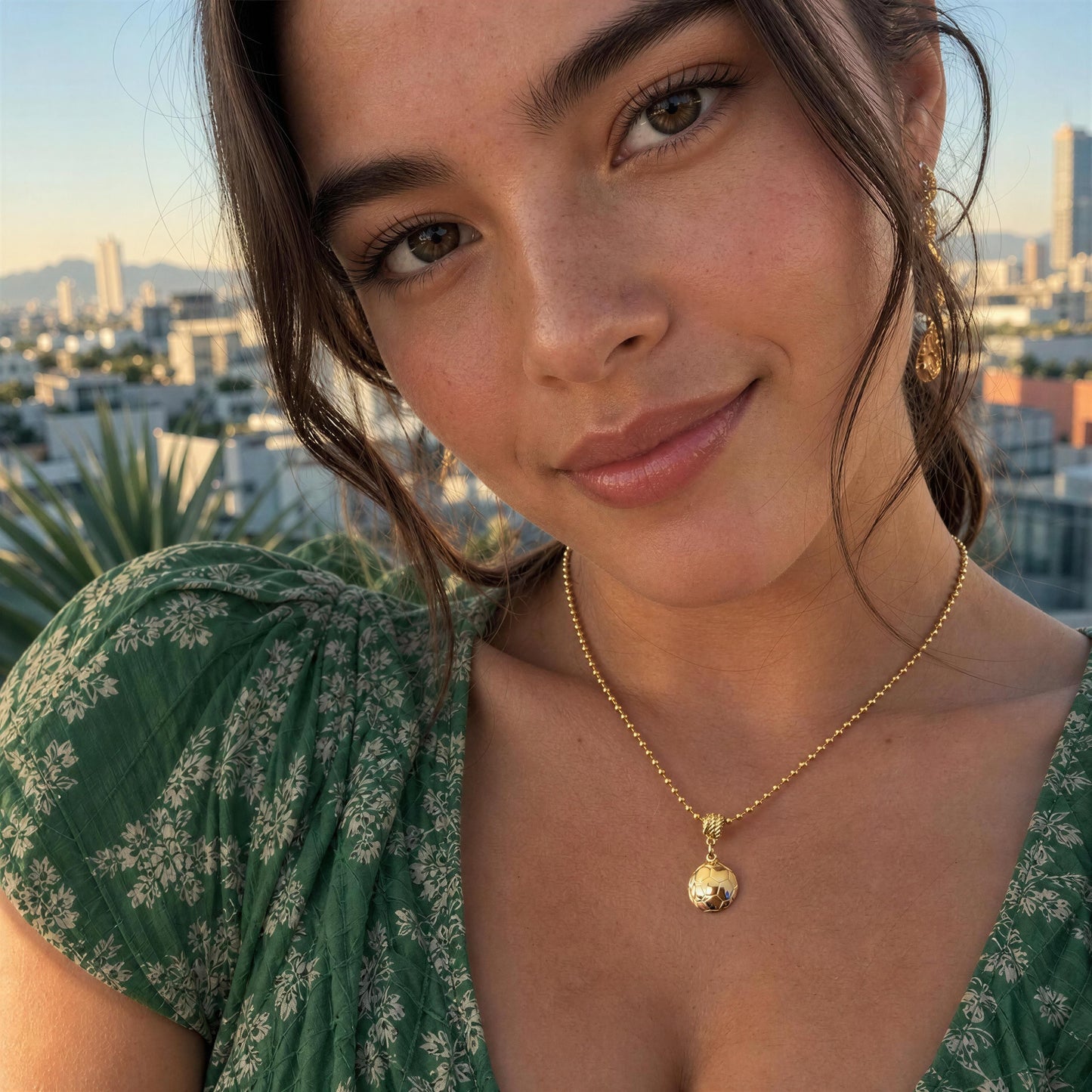 Woman wearing a green floral dress with the Gol Dorado Necklace, standing outdoors with a cityscape in the background.
