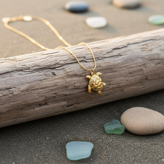 Golden Harbor Turtle Necklace on a piece of driftwood with beach stones in the background