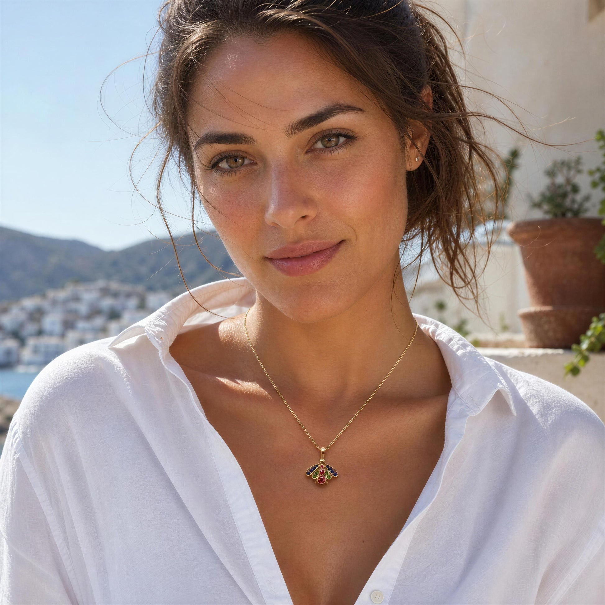 A woman wearing the Golden Meadow Bee Necklace and background of a coastal town.
