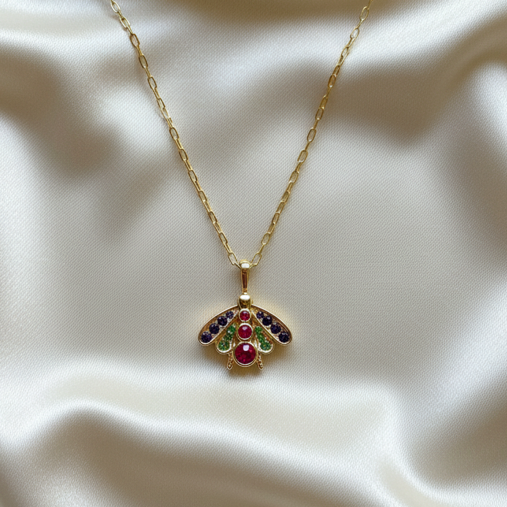 Gold Chica Chica Jewelry necklace with a colorful pendant on a beige fabric background