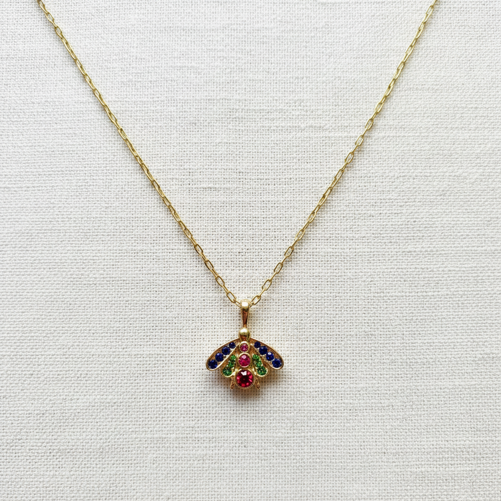Gold Chica Chica Jewelry necklace with a colorful bee-shaped pendant on a light gray background