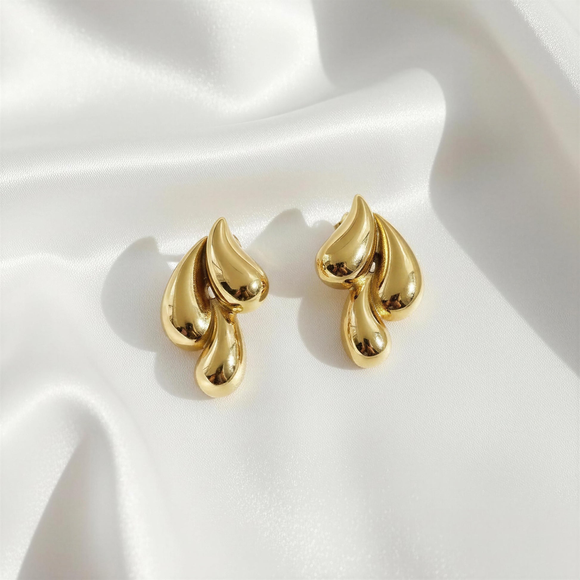 Gold sculptural drop earrings on silk fabric with soft highlights