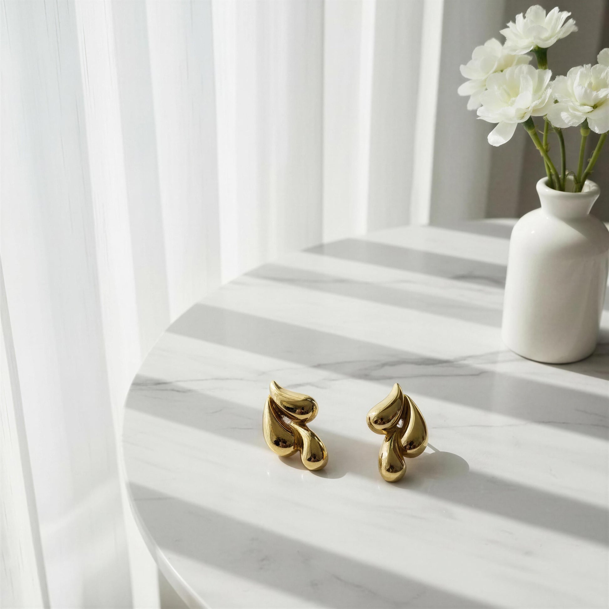 Sculptural gold earrings on marble table with soft shadows
