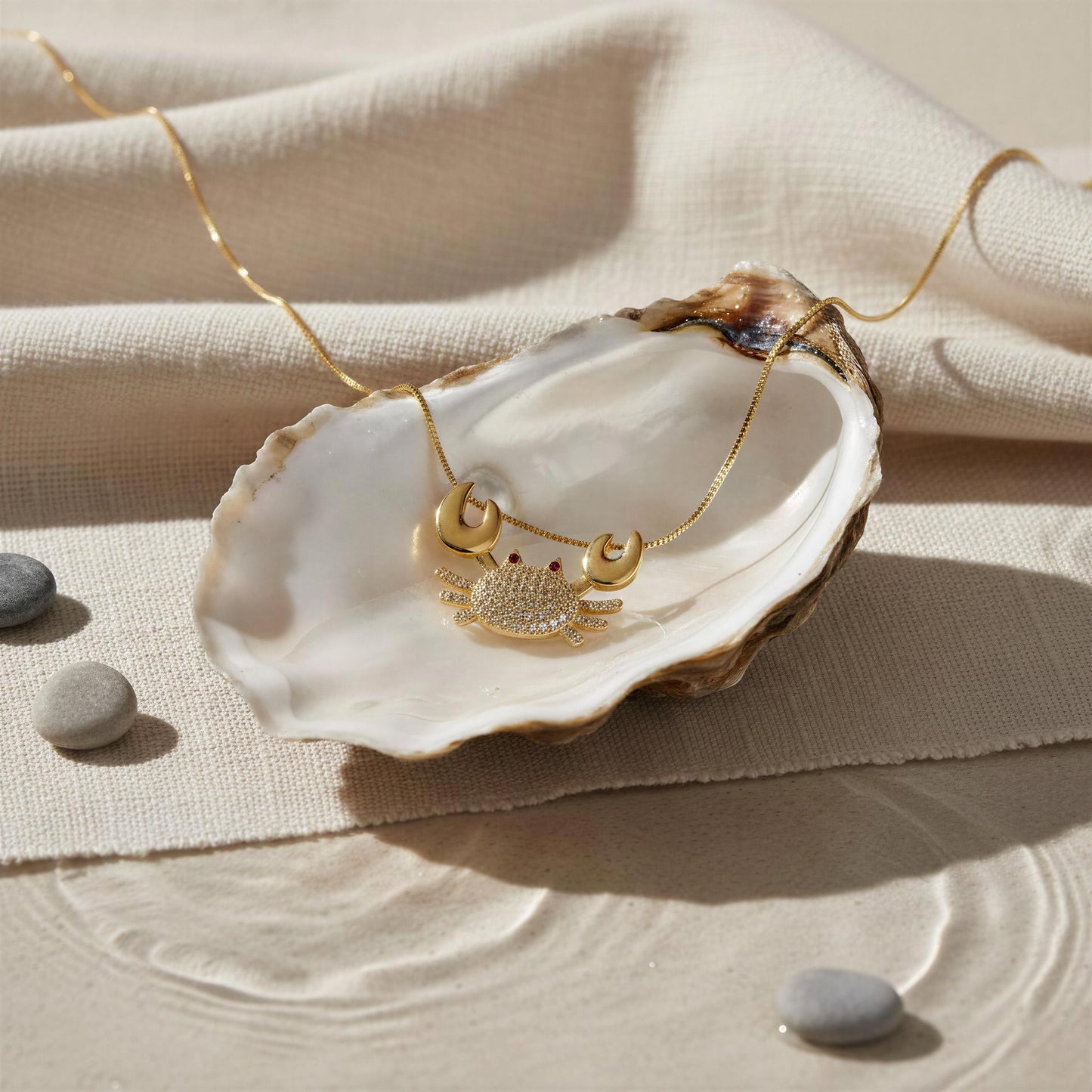 The Golden Tides Crab Necklace from Chica Chica Jewelry  on an open shell against a beige fabric background.