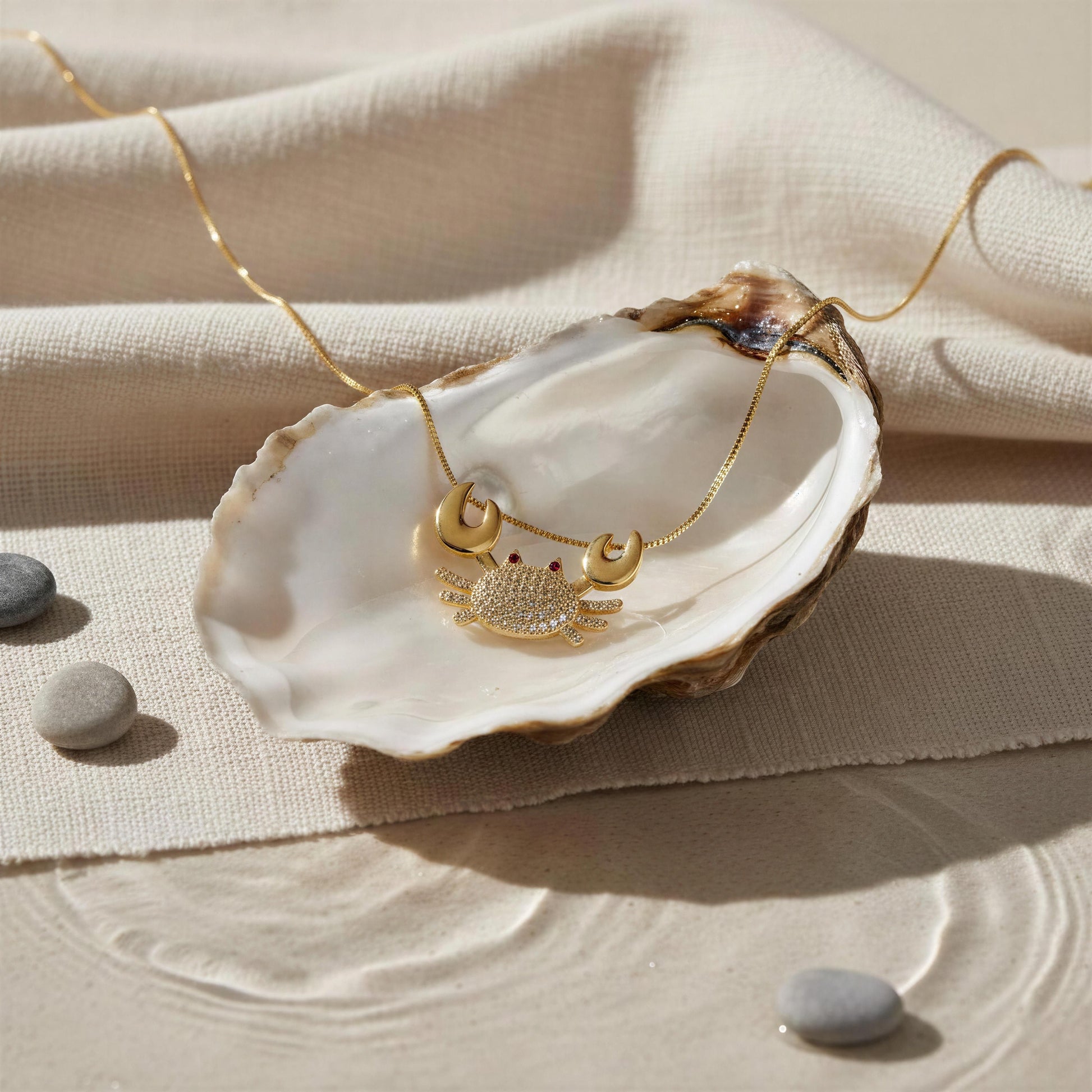 The Golden Tides Crab Necklace from Chica Chica Jewelry  on an open shell against a beige fabric background.