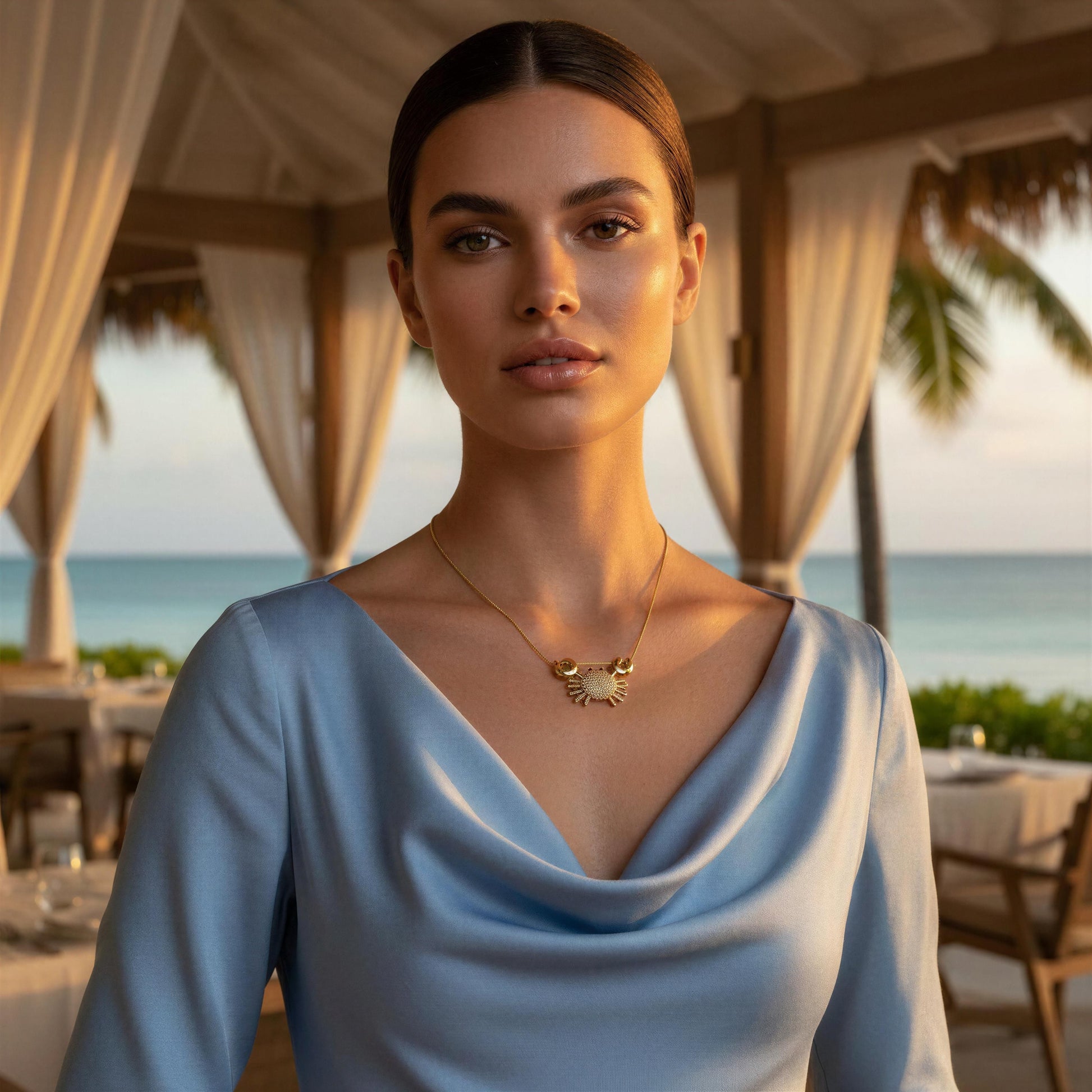 Woman wearing a blue dress with the Golden Tides Crab Necklace  in an outdoor setting with ocean view