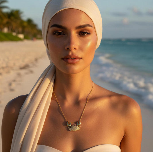 Woman on a beach wearing a white headscarf and the Golden Tides Crab Necklace with a sunset background