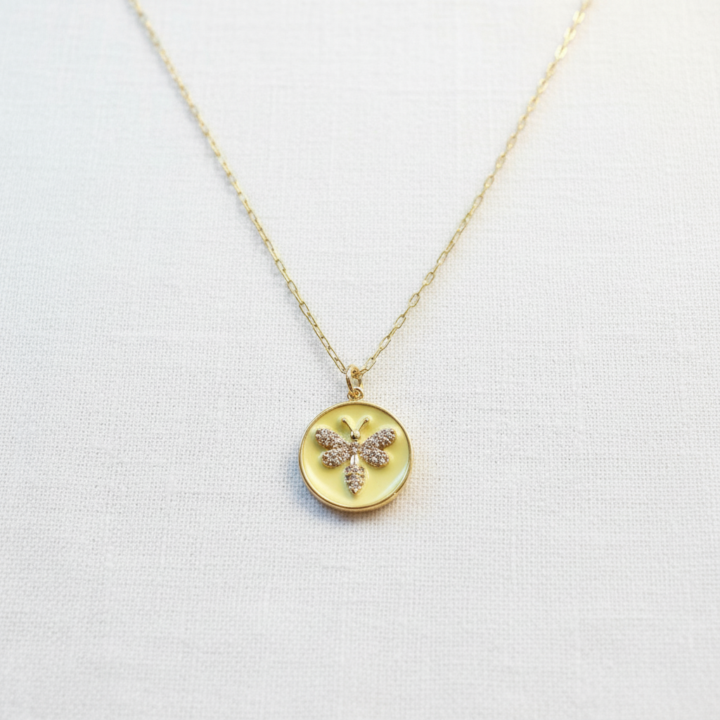 Gold necklace with a round pendant featuring a butterfly design on a light gray background- from Chica Chica Jewelry