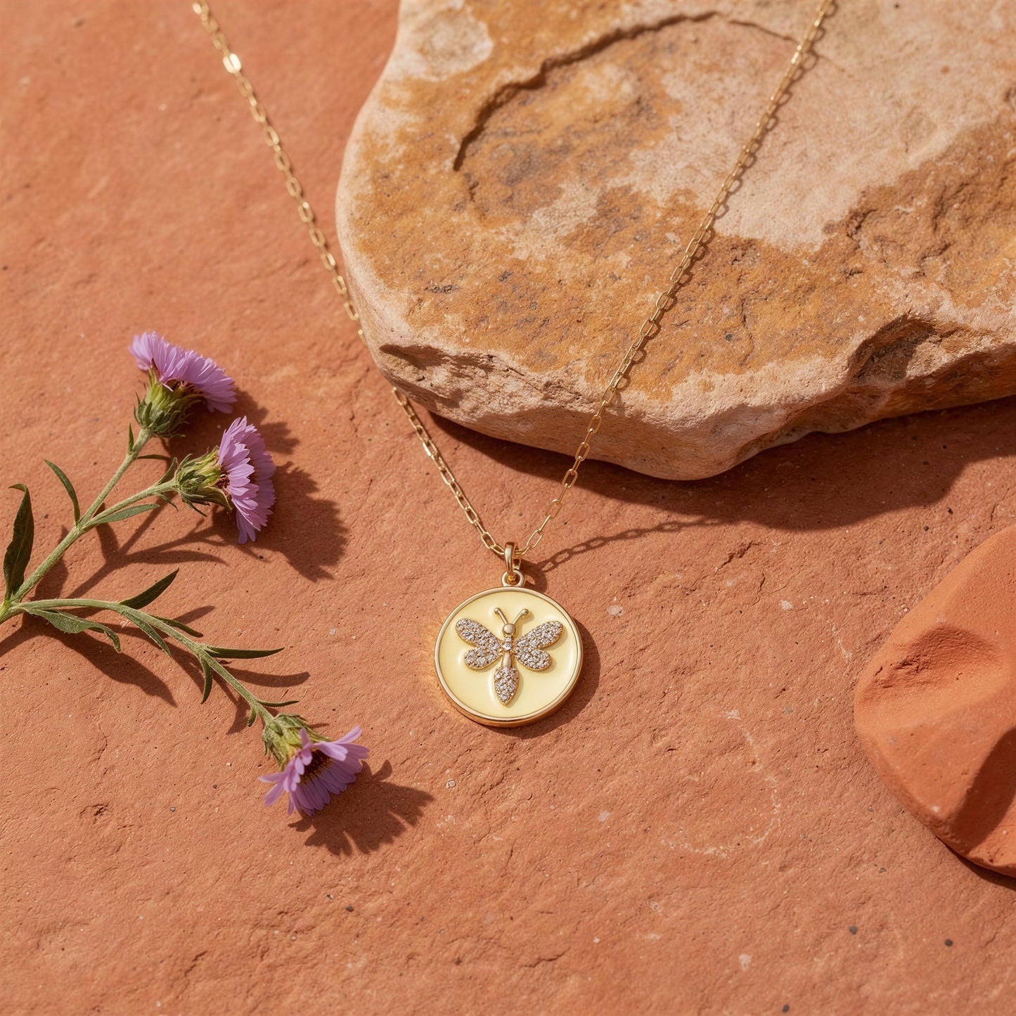 Gold necklace with a butterfly pendant on a stone surface with purple flowers
