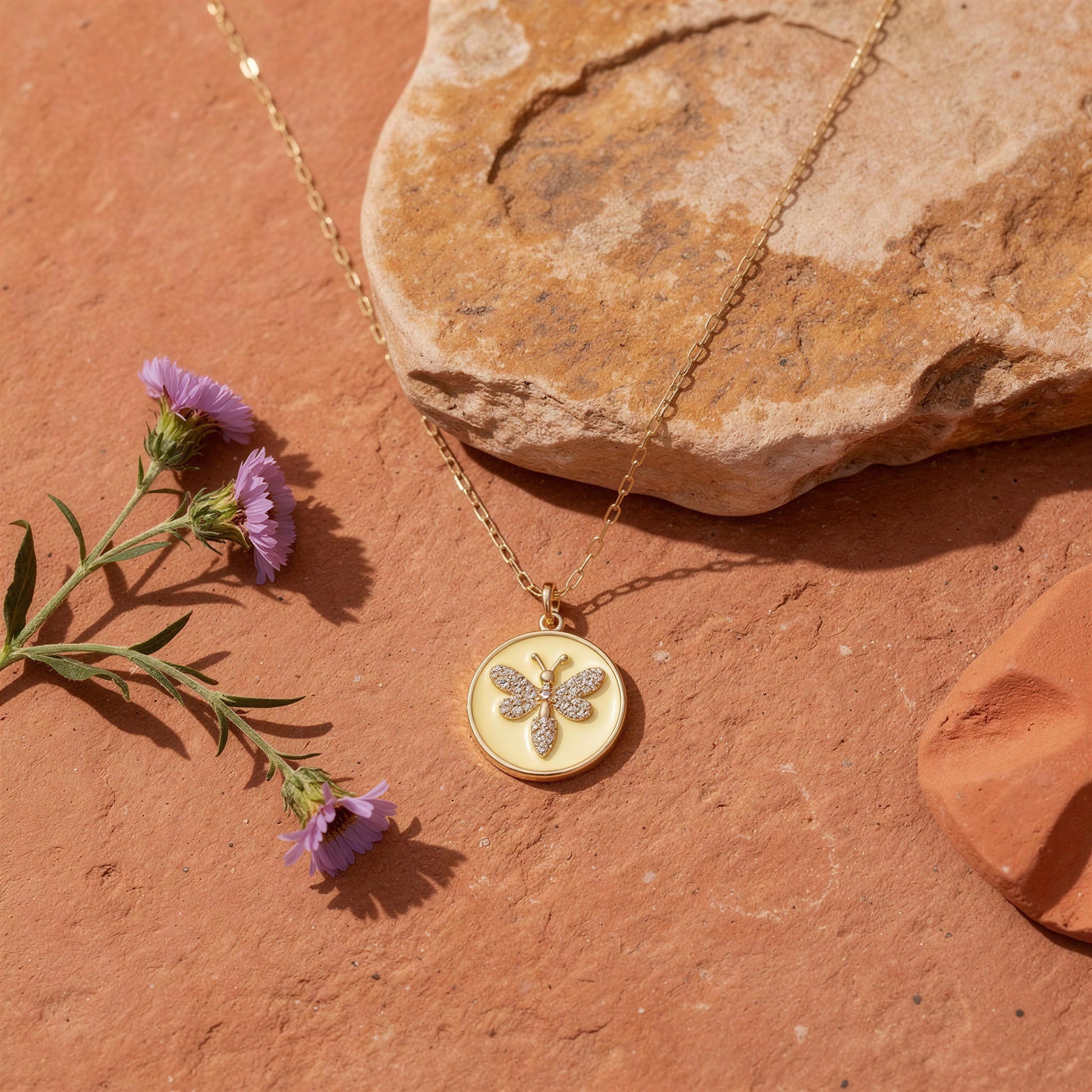 Gold necklace with a butterfly pendant on a stone surface with purple flowers