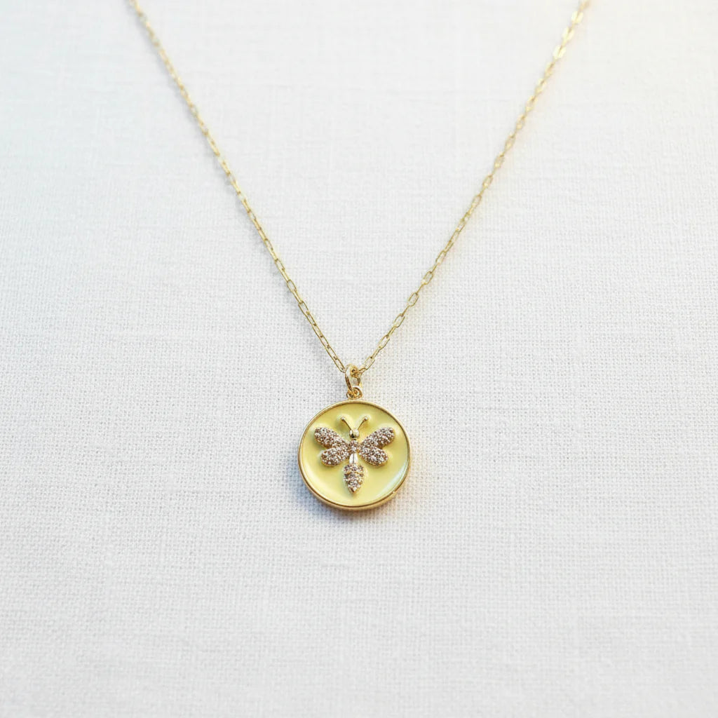 The Golden Wasp Medallion Necklace with round pendant featuring a butterfly design on a light gray background