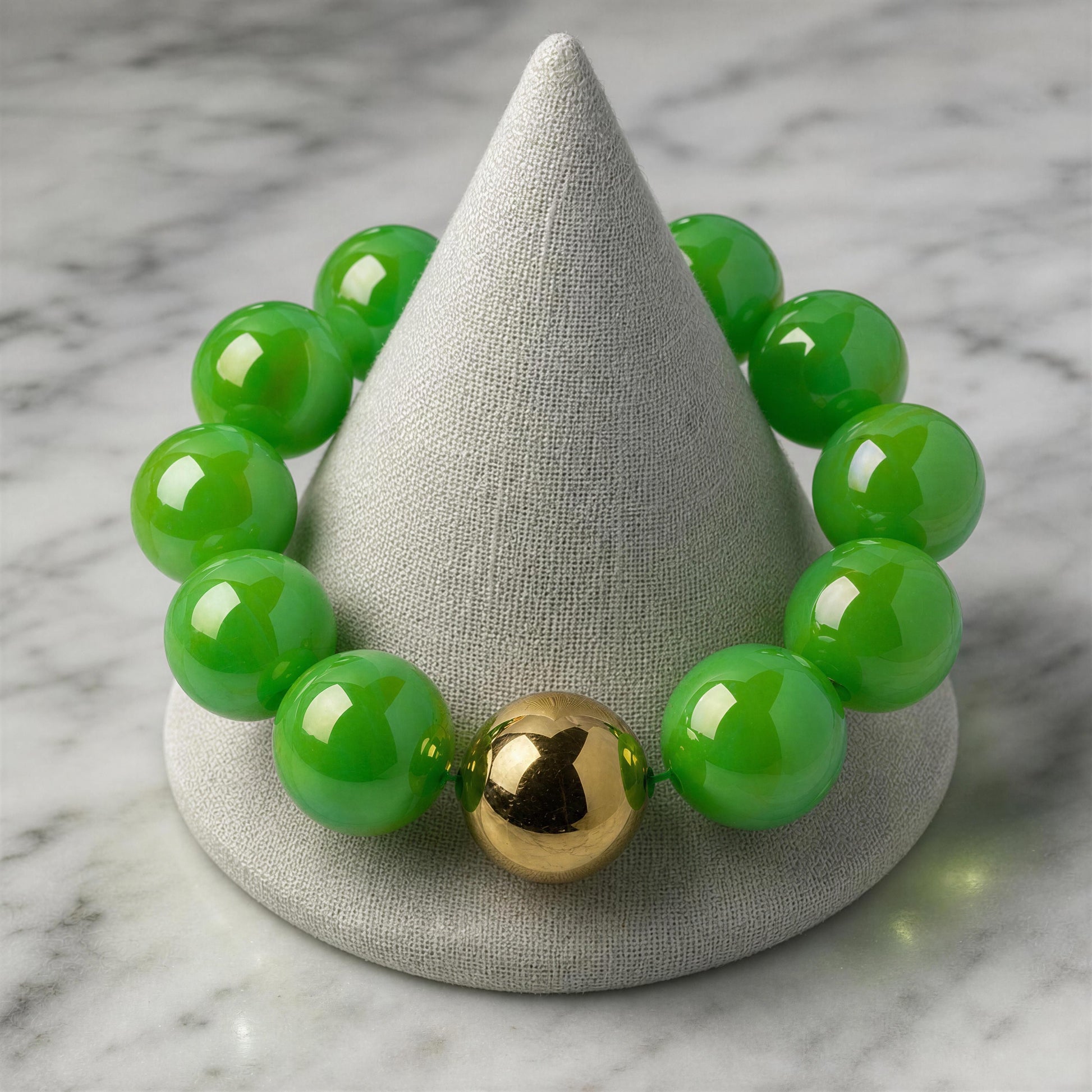 Green beaded bracelet with a gold accent on a gray cone-shaped stand against a marble background