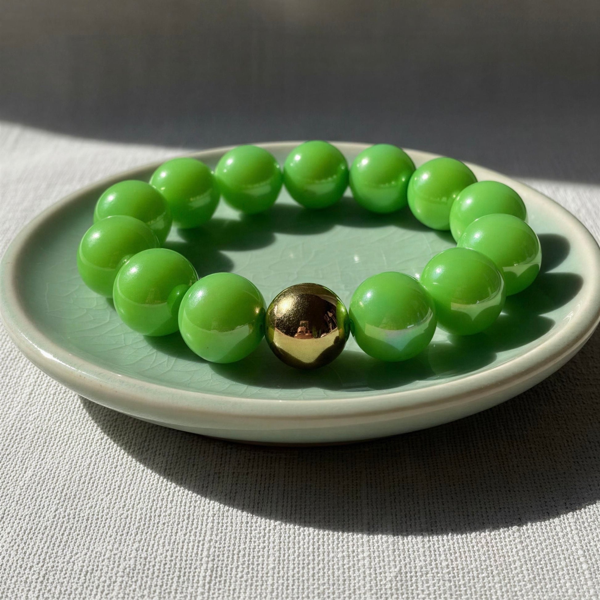 Green beaded bracelet with a gold bead on a light green plate.