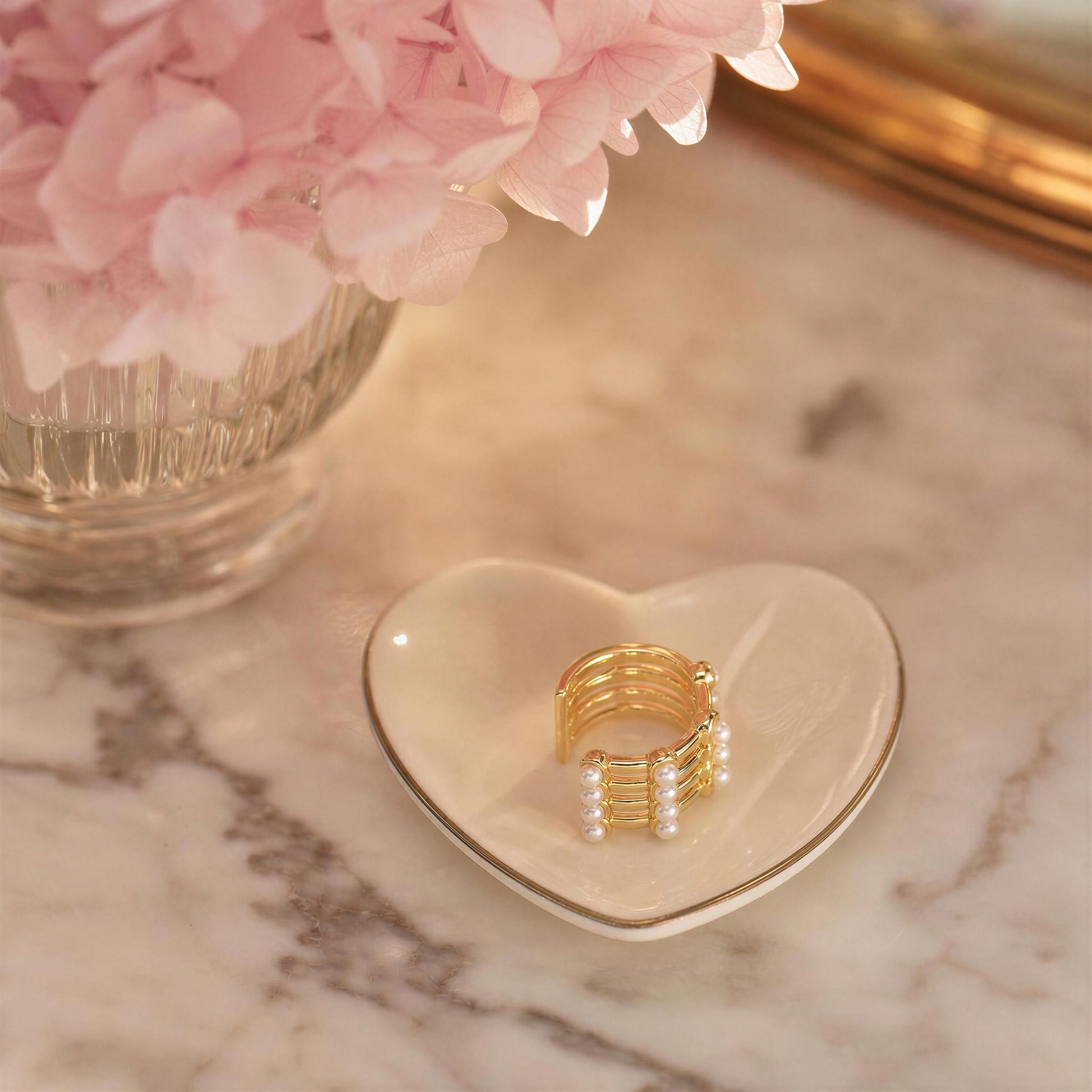 The Grid Pearl Ear Cuff on a heart-shaped dish with pink flowers in the background