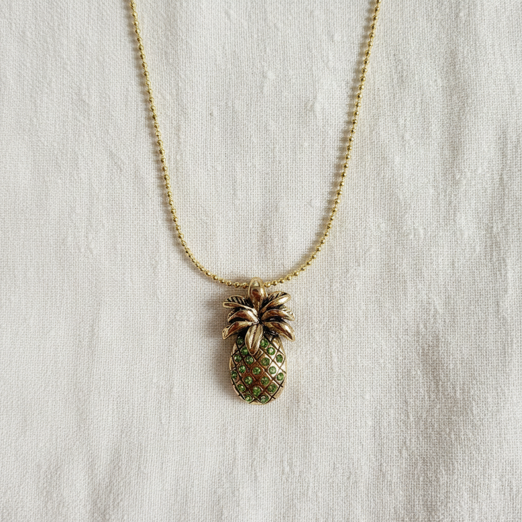 Pineapple-shaped pendant on a chain against a light fabric background