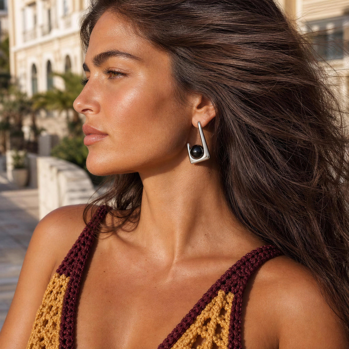 A woman in profile wearing the Kara Earrings from Chica Chica Jewelry, a silver-toned geometric drop earring with a black circular center, photographed outdoors in warm sunlight.