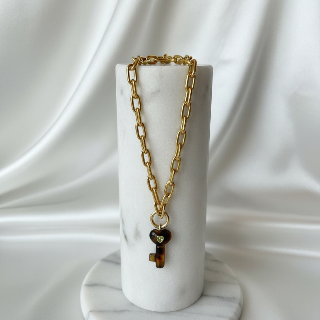 La Vita Forte – Tigre with a key-shaped pendant on a marble stand against a white draped fabric background