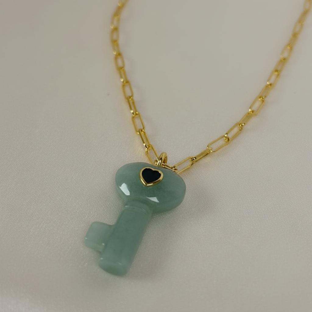 Necklace with a green key-shaped pendant on a gold chain against a light background