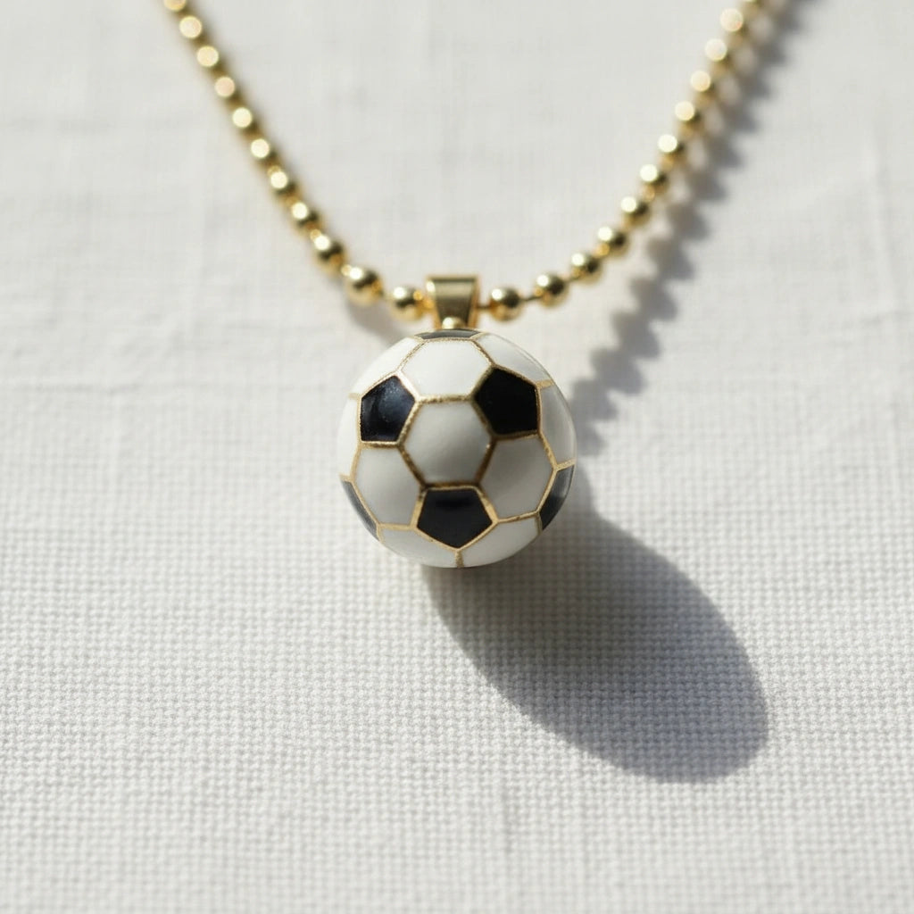 Detailed close-up of black and white enamel soccer ball charm with gold border on an 18K gold-plated chain