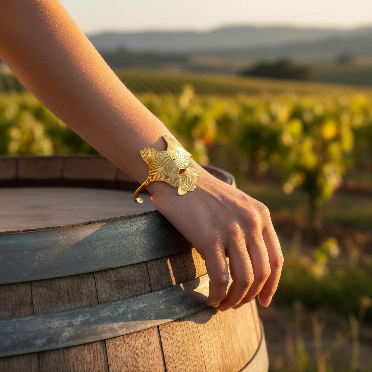 Hand wearing the Leaf of Eternity Cuff Bracelet
from Chica Chica Jewelry on a wooden barrel in a vineyard setting