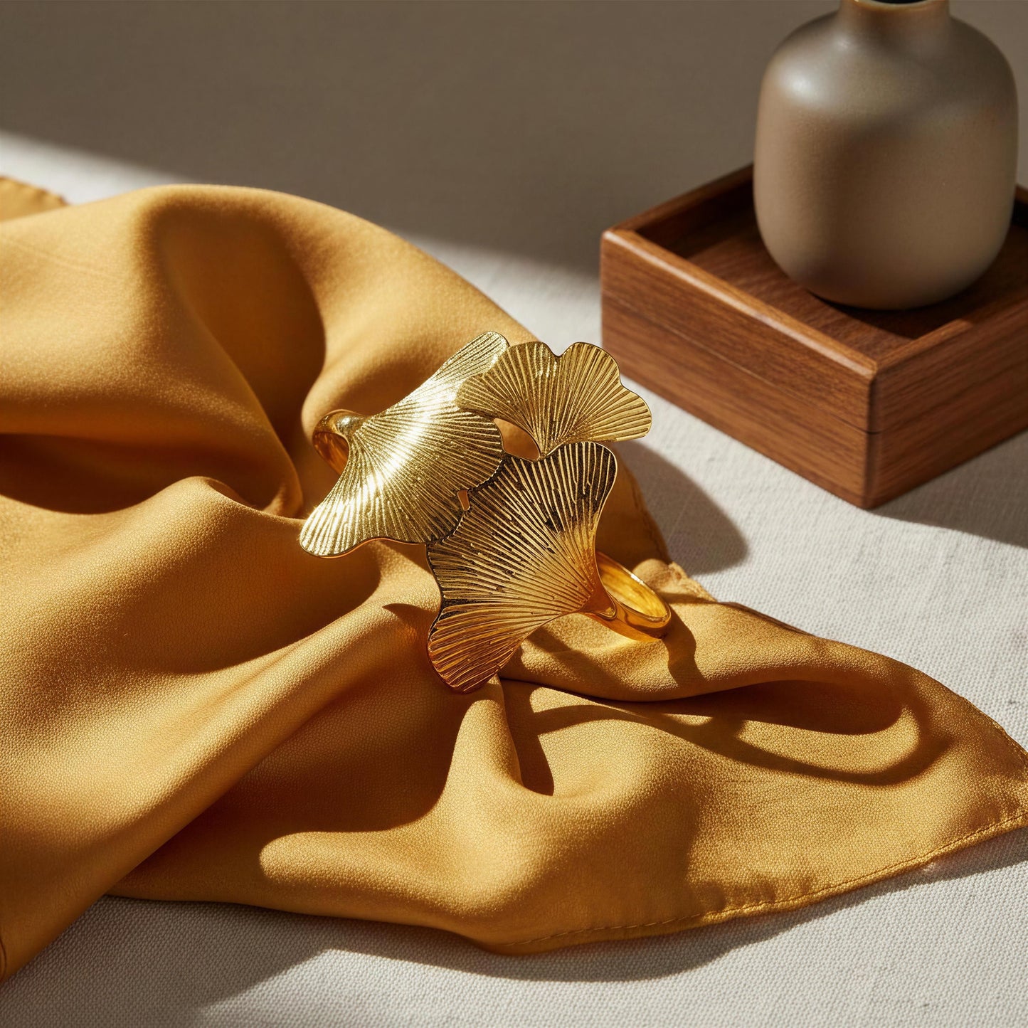 The Leaf of Eternity Cuff Bracelet on a yellow fabric with a wooden box and beige vase in the background.
