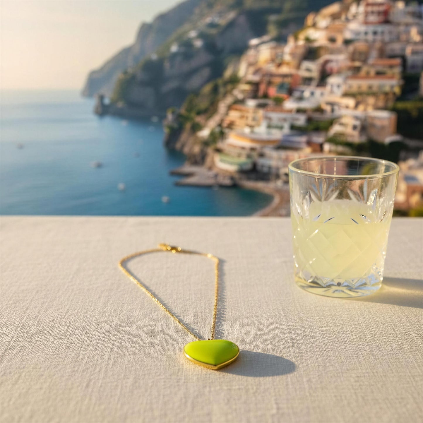 Glass of lemonade with the Limoncello Heart Necklace on a table with a scenic background.