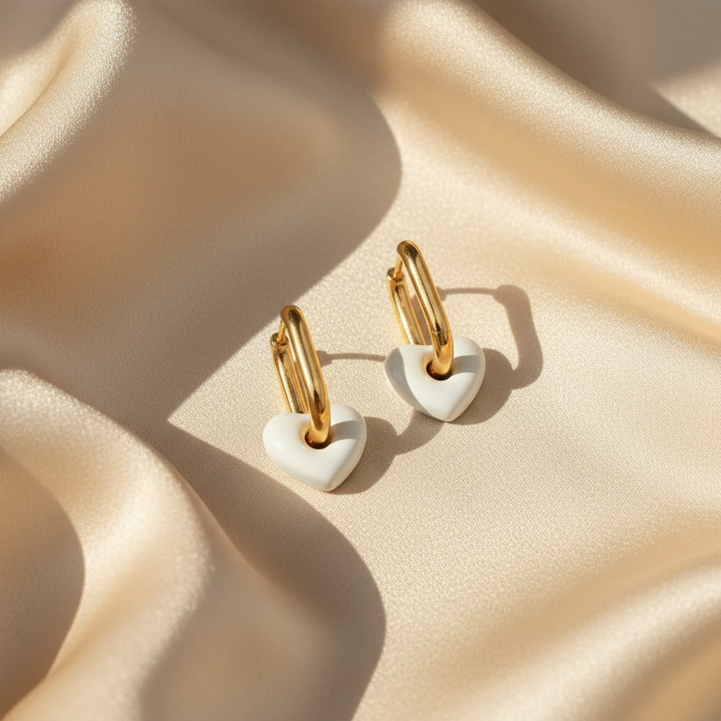 Gold hoop earrings with white heart-shaped ends on a beige fabric background