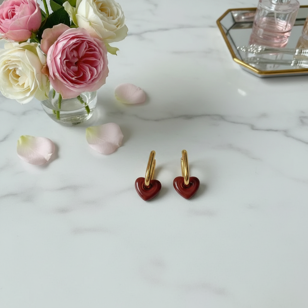 Heart-shaped earrings on a marble surface with pink roses in the background