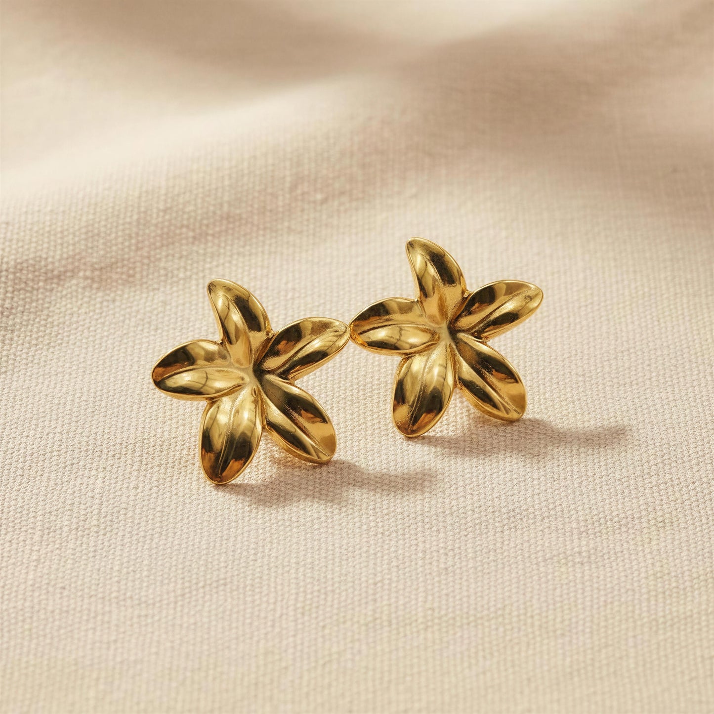 Pair of gold flower-shaped earrings on a beige fabric background