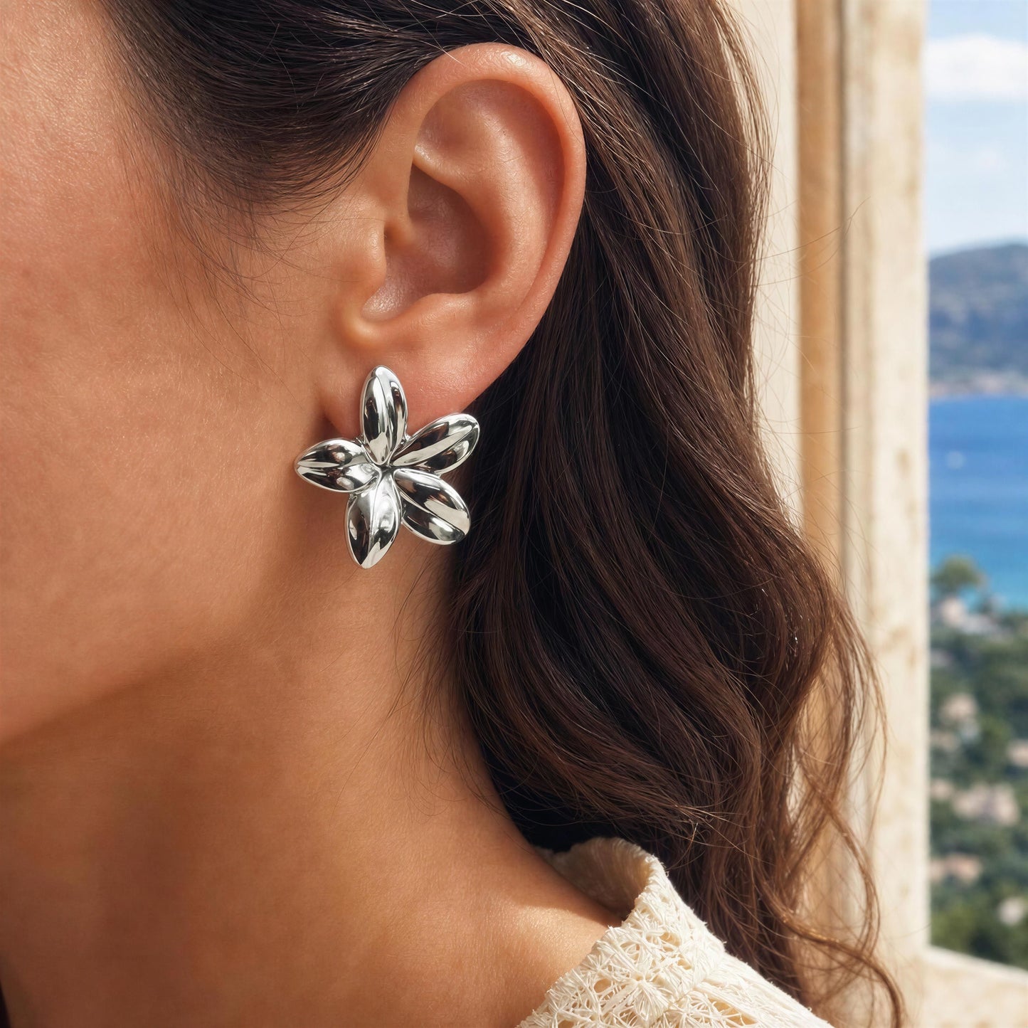 Silver flower-shaped earring worn by a person with a scenic background