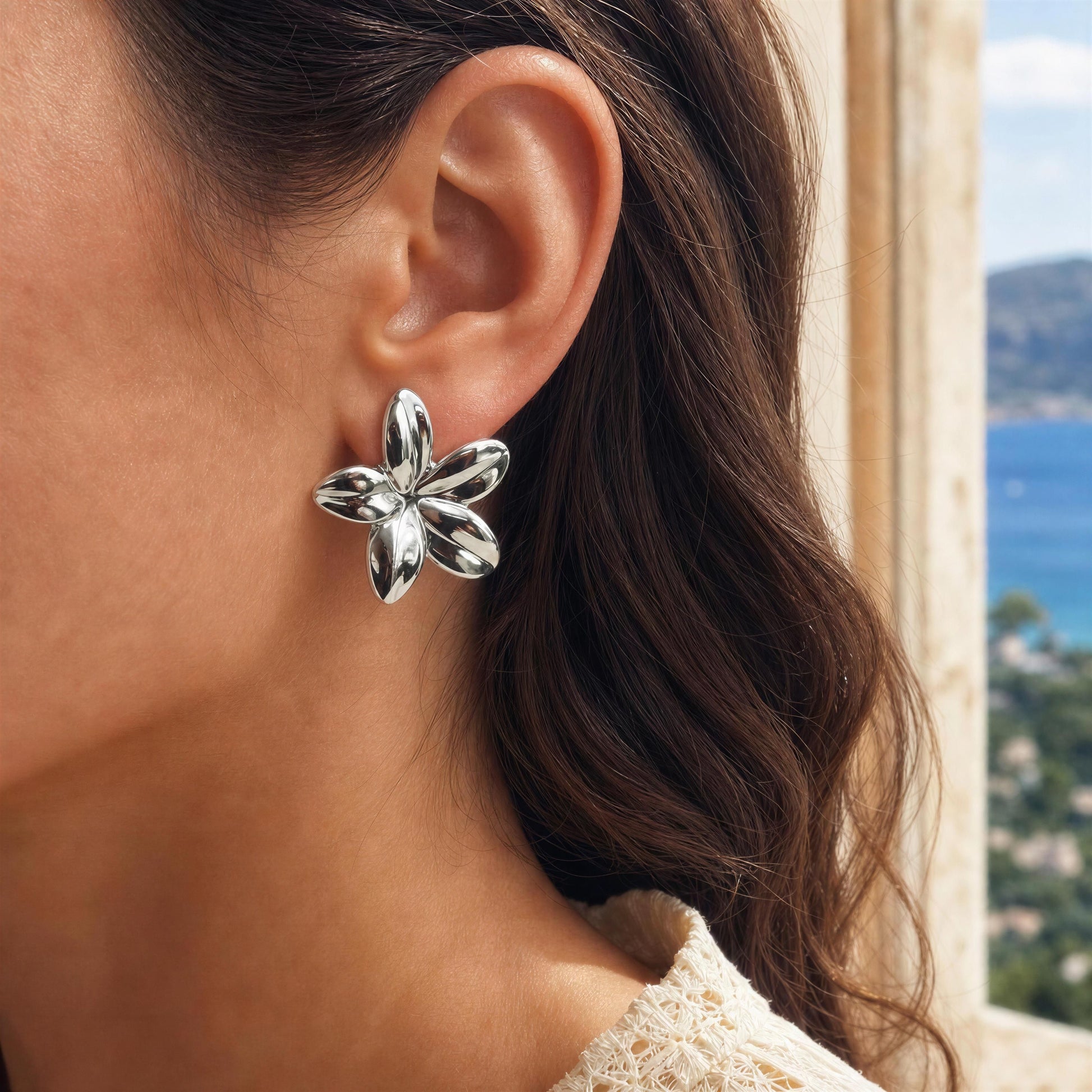 Silver flower-shaped earring worn by a person with a scenic background