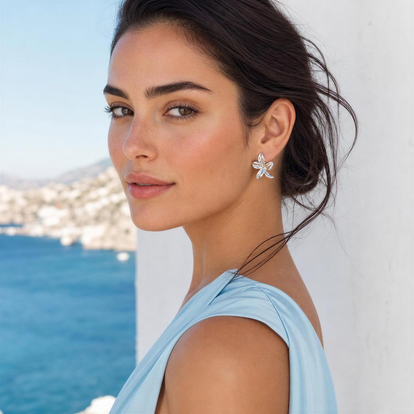 Woman wearing a light blue dress and the Luna Bloom Earrings - Silver with ocean view in the background