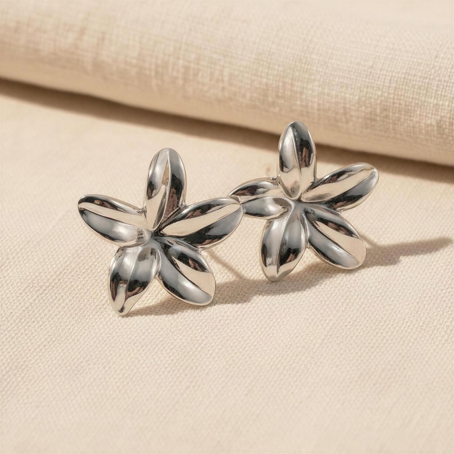 The Luna Bloom Earrings - Silver  on a beige fabric background